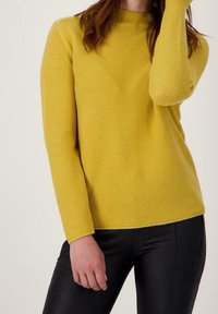 Żółty sweter z prążkowanym wzorem, posiadający długie rękawy i okrągły dekolt, zestawiony z czarnymi spodniami slim-fit, podkreślającymi bogaty w tekstury design.