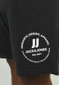 Shorts en coton noir avec un logo circulaire blanc portant le texte "JACK & JONES", des accents graphiques et des détails de couture.