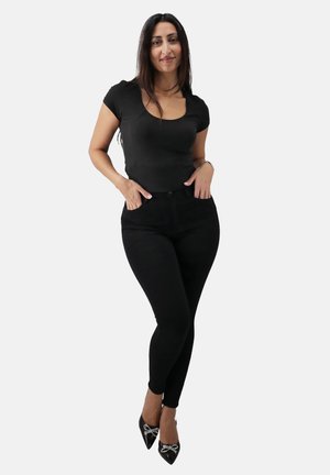 Black fitted T-shirt with short sleeves, paired with high-waisted black pants. Shoes are black with jeweled accents in a pointed style.