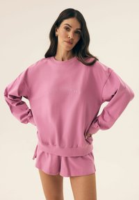 Różowa bluza z dekoltem okrągłym i haftowanym napisem "West Virginia", zestawiona z pasującymi różowymi szortami. Wykonana z miękkiego bawełnianego materiału.