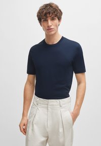 Mørk marineblå kortermet T-skjorte laget av glatt stoff, rund hals, tettsittende design, brukt med lyse plisserte bukser.
