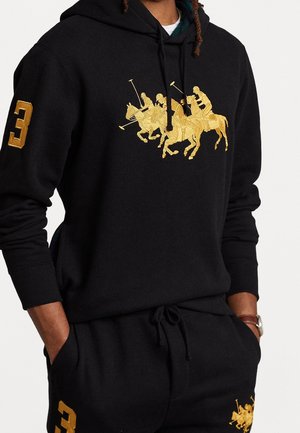 Schwarzes Hoodie- und Hosenset mit goldbestickten Polospielern auf Brust und Oberschenkel, goldene Nummer drei auf dem linken Ärmel und rechten Oberschenkel.