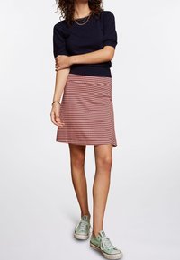 Granatowy sweter z krótkim rękawem połączony z czerwono-białą spódnicą w kształcie litery A i zielonymi sneakersami. Gładka tekstura, swobodny design.