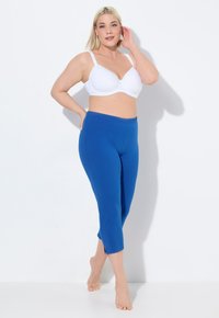 Niebieskie, elastyczne spodnie capri z bocznymi rozcięciami, zestawione z białym, usztywnianym biustonoszem. Miękki materiał, dopasowany krój i elastyczny pas.