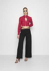 Blusa cropped com padrão vermelho, abertura em forma de buraco na frente e mangas bufantes, combinada com calças largas pretas e saltos pretos com tiras.