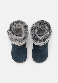 Tmavě modré semišové boty se šedým umělým kožíškem na horním okraji a podšívce. Zaoblená špička a plochá podrážka. Vložka obsahuje vytištěné logo.