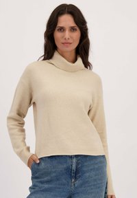 Beige trui met een col, lange mouwen en ribgebreide manchetten. Gemaakt van zacht materiaal, heeft een losse pasvorm met een cropped zoom.