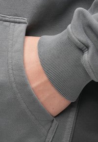 Dark gray sweatshirt featuring a ribbed cuff and hand in a front pocket, showcasing fabric texture and stitching details.