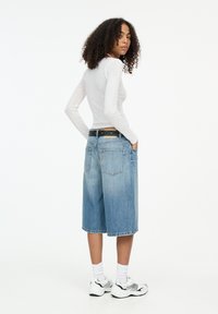 Maglione grigio chiaro a maniche lunghe, culotte in denim blu con una vestibilità rilassata, due tasche posteriori e cintura nera con accenti argentati. Sneakers bianche e calze.