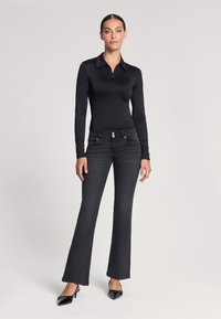 Polo a maniche lunghe nera abbinata a jeans a zampa d'elefante grigio scuro. Tacchi neri lucidi valorizzano la silhouette moderna e la vestibilità dell'outfit.