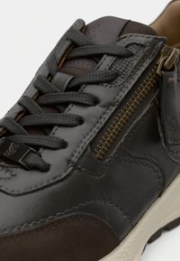 Tume nahk sneaker, millel on tekstureeritud pind, kontrastsed pruunid aktsendid, vastupidavad paelad, külgne tõmblukk ja valge kummist tald.