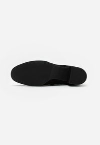 Suela de zapato negra con una textura suave y sutiles surcos horizontales, que presenta un diseño afilado y un tacón ligeramente elevado.