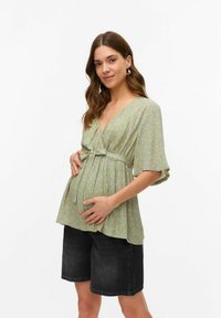 Zelena cvetna bluzica za noseče z V-izrezom, kratkimi rokavi in pasom na zavezovanje. Ujemite jo z črnimi denim kratkimi hlačami, ki imajo ohlapen kroj.