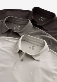 Tre polo shirt impilati: marrone scuro, verde oliva e beige chiaro. Ognuno ha un colletto, dettagli con bottoni e un motivo ricamato sul petto.