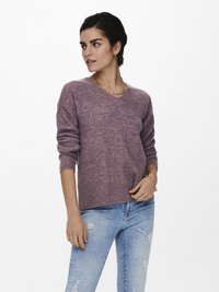 V-Ausschnitt, langärmeliger Pullover aus einem strukturierten, lavendelfarbenen Strickstoff. Kombiniert mit hellen, verwaschenen Jeans, die dezente Risse und fransige Säume aufweisen.