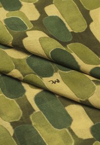 Tissu à motifs comprenant de grandes formes ovales lisses dans des teintes de vert et de jaune. Texture douce avec un logo visible dans le coin.