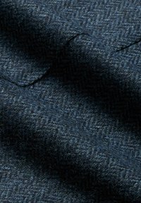 Tessuto di lana blu scuro con un motivo a spina di pesce, caratterizzato da una consistenza morbida e una leggera lucentezza, con fibre visibili in tutto il tessuto.