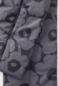 Veste matelassée en tissu gris foncé présentant un grand motif floral dans différentes nuances de gris. Texture lisse, avec des détails de couture visibles.