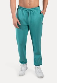 Teal sweatpants met een elastische tailleband, trekkoord, zijzakken en geribbelde manchetten, gecombineerd met witte sneakers. Zachte stoftextuur.
