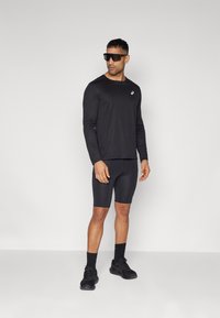 Sort langærmet træningsshirt med et lille logo, parret med sorte kompressionsshorts og sorte træningssko. Accessories inkluderer solbriller.