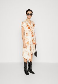 O rochie cu mâneci scurte dintr-un material portocaliu deschis și alb, cu modele abstracte, asortată cu cizme negre până la genunchi și o mică geantă neagră.