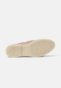 Zapato de ante rosa con suela de goma beige, que presenta un patrón texturizado, bordes ondulados y puntos de agarre circulares en la parte inferior.