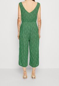 Groene, geprinte jumpsuit met een V-rug, wijde benen en een toegespitste taille. Kenmerkend zijn kleine, donkere patronen en een lichte stoftextuur.