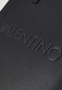Czarny materiał teksturowany z wytłoczonym logo "VALENTINO". Czyste linie i minimalistyczny design. Subtelny wzór na powierzchni.