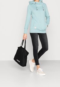 ljusblå huvtröja med dragsnören, tillsammans med svarta skinny jeans och beige sneakers. Svart tote-väska med vitt logo.