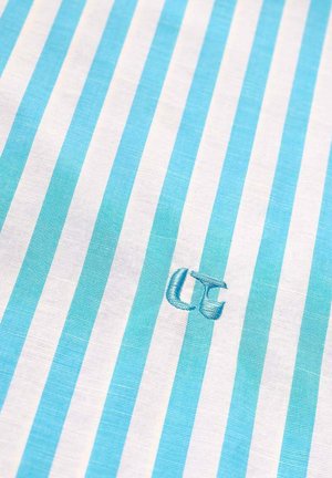 Tissu à rayures verticales bleues et blanches avec les initiales "UC" brodées en bleu près du centre.