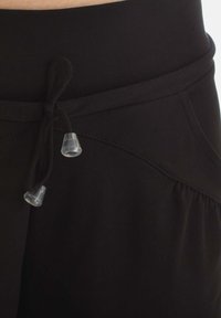Black relaxed-fit sweatpants with a smooth texture, elastic waistband, and a drawstring featuring transparent tips.