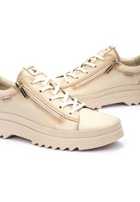 Sneaker in pelle beige con finitura testurizzata, dotati di una chiusura con zip e allacciatura frontale, montati su una suola in gomma spessa.