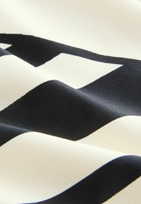 Tissu noir et blanc à motifs avec une texture lisse, présentant de grandes formes géométriques et un drapé fluide.