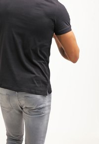 T-shirt noire ajustée à manches courtes, en tissu lisse, avec des détails de couture visibles, associée à un jean slim gris clair.