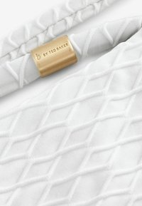 Tessuto bianco con un motivo a diamante testurizzato. Presenta un accento metallico dorato con marchio inciso. Texture morbida e liscia.