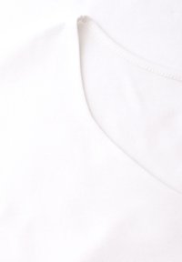 Zbliżenie na biały materiał ubrania z widocznym dekoltem i przeszyciem na szwie.