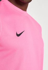 Ροζ αθλητική μπλούζα Nike μ ε υφή, διαθέτει στρογγυλή λαιμόκοψη και μαύρο λογότυπο swoosh στην αριστερή πλευρά του στήθους.