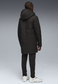 Svart huva parka med kviltad textur, som sträcker sig nedanför höfterna, kombinerad med mörka sweatpants och vita sportskor.