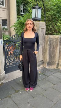 Top nero a maniche lunghe con scollatura quadrata, abbinato a pantaloni a gamba larga ad alto ventre. Gli accessori includono una borsa nera e sneakers rosa.