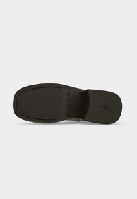 Semelle d'une chaussure habillée en cuir marron foncé avec un bout carré et un petit logo embossé sur le talon.
