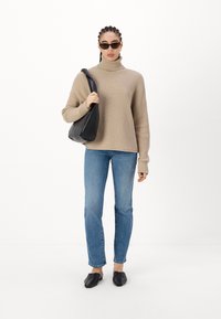 Suéter beige de cuello alto con canalé, jeans azul claro, mules negros y un bolso negro de hombro. Mangas distintivas y tejido texturizado.