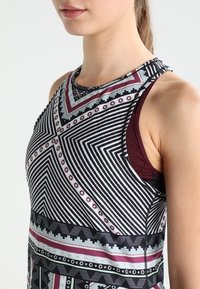 Bezrukávý sportovní top s geometrickým černobílým vzorem a akcenty v barvách burgundy a máty. Vyrobeno z lehkého, prodyšného materiálu.