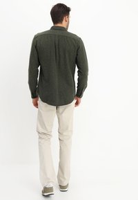 Dark green, speckled button-up shirt with long sleeves and a back yoke, paired with light beige pants and gray-green sneakers.