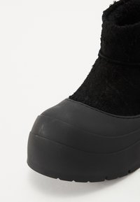 Botă neagră cu un superior texturat, talpă din cauciuc, vârf rotund și un design gros și rezistent. Prezintă o estetică elegantă și minimalistă.