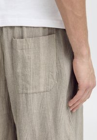 Beige striped pants with a textured fabric, featuring a single rear pocket and a relaxed fit. The stripes alternate between light and dark tones.