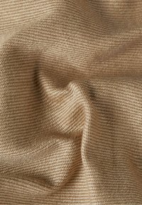 Tela tejida de color beige claro con una superficie texturizada, que presenta un ribeteado diagonal y variaciones sutiles en el color, indicativas de fibras naturales.