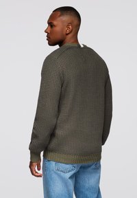 Suéter de punto verde oliva con patrón texturizado, cuello redondo, puños y dobladillo acanalados. Combinado con jeans de mezclilla azul claro.