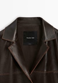 Braune Lederjacke mit einem Reverskragen, versehen mit einem schwarzen Etikett mit der Aufschrift "Massimo Dutti" innen. Die Textur ist glatt mit sichtbaren Nähten.