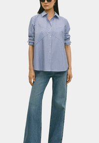 Blauw en witte gestreepte overhemden met kraag, voorzien van een gebogen yoke-ontwerp en opgerolde mouwen, gedragen met wijde spijkerbroeken.