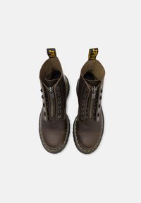 Botas de cuero marrón con cierre de cremallera y cordones, costuras amarillas y una suela de goma resistente. Diseñadas con una punta redondeada y una lengüeta en la parte posterior.